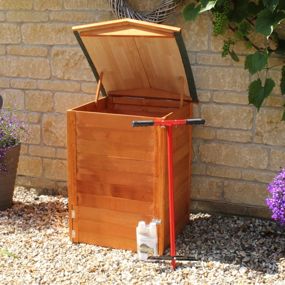 Wooden compost bin with a red aerator against a stone wall.