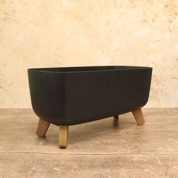 A black, concrete trough-style plant pot with wooden legs, containing various plants