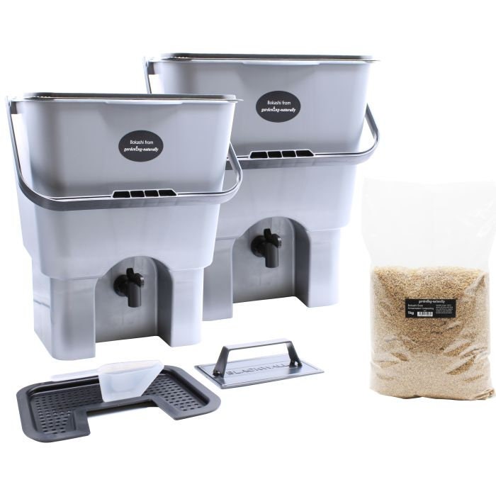 Two gray Bokashi compost bins with airtight lids, accompanied by a bag of Bokashi Bran, a scoop, and two taps.