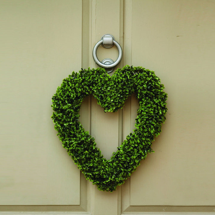 A boxwood heart-shaped wreath hanging on a door frame.