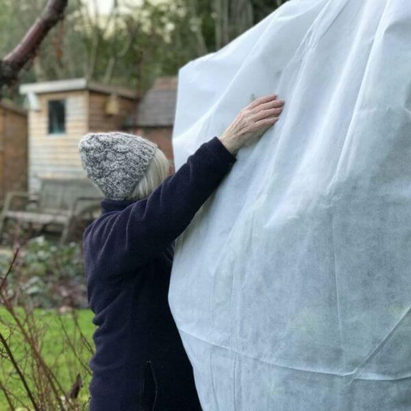 Person holding a large white sheet outdoors with a garden and shed in the background