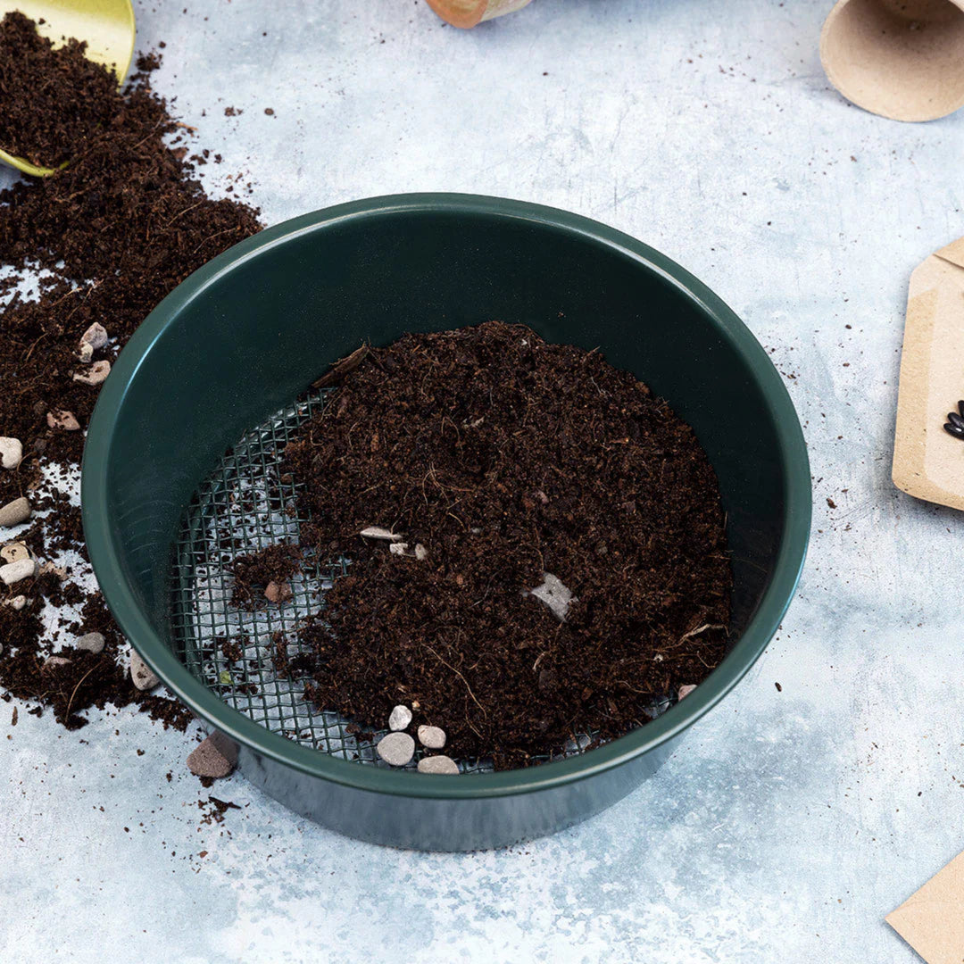 Soil sieve on greenhouse bench full of compost and a few stones