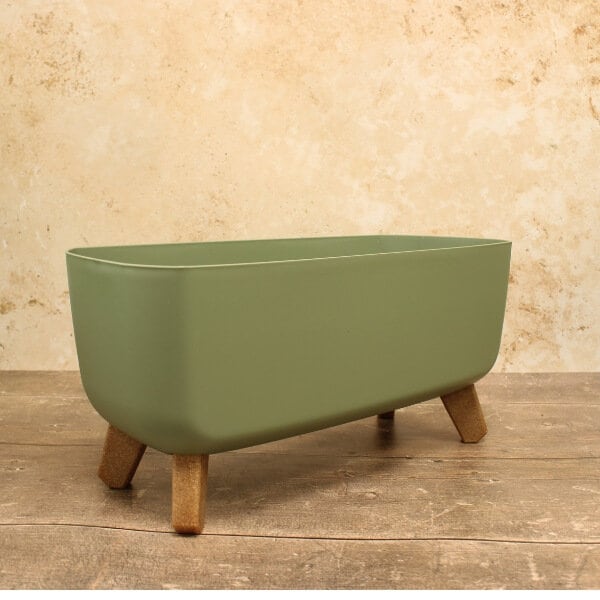 A green, concrete trough-style plant pot with wooden legs, empty