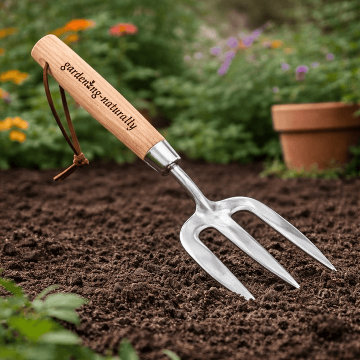 A small hand garden fork with a natural wood handle engraved with 'Gardening-naturally' and a brown leather loop, 