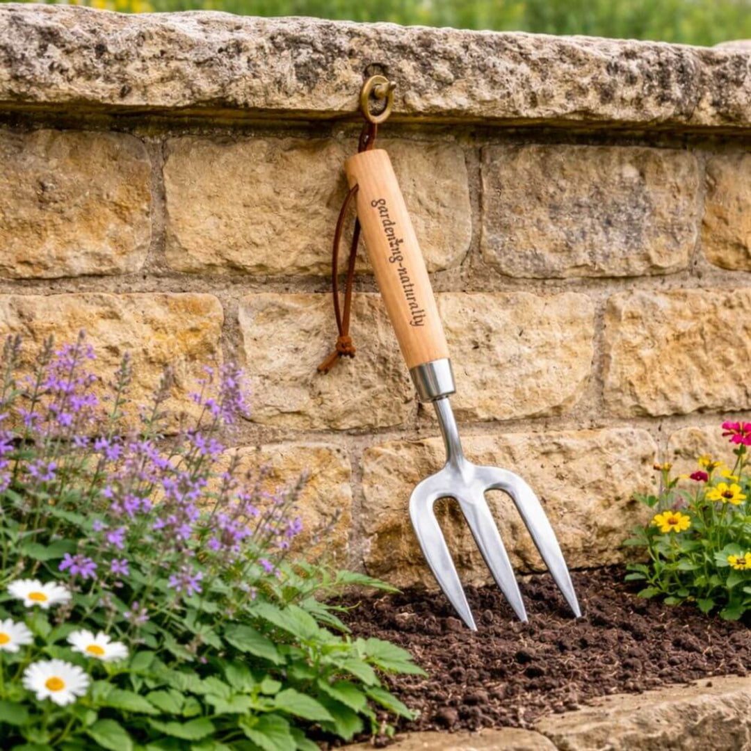 Gardening fork with wooden handle hanging on a stone wall with flowers in the foreground