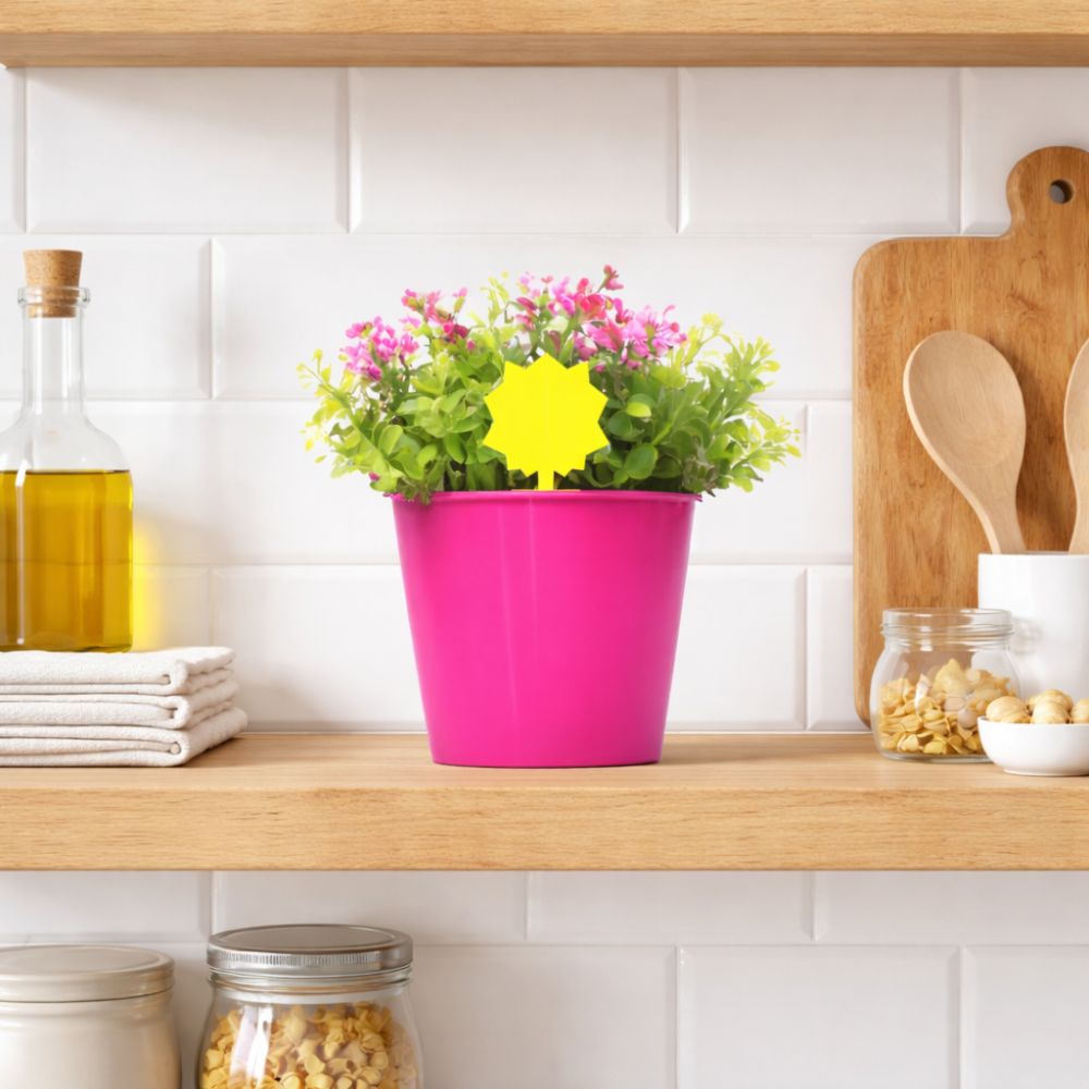 Pink flowerpot with flowers on a kitchen shelf with various items.