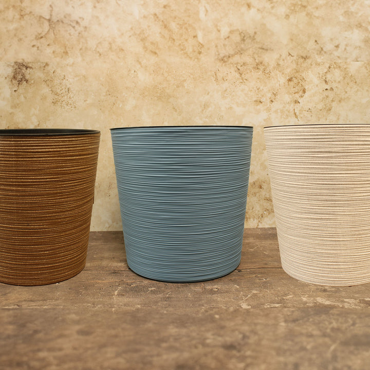Three round, recycled flowerpots placed side by side. From left to right, the pots are brown, blue, and white in color.