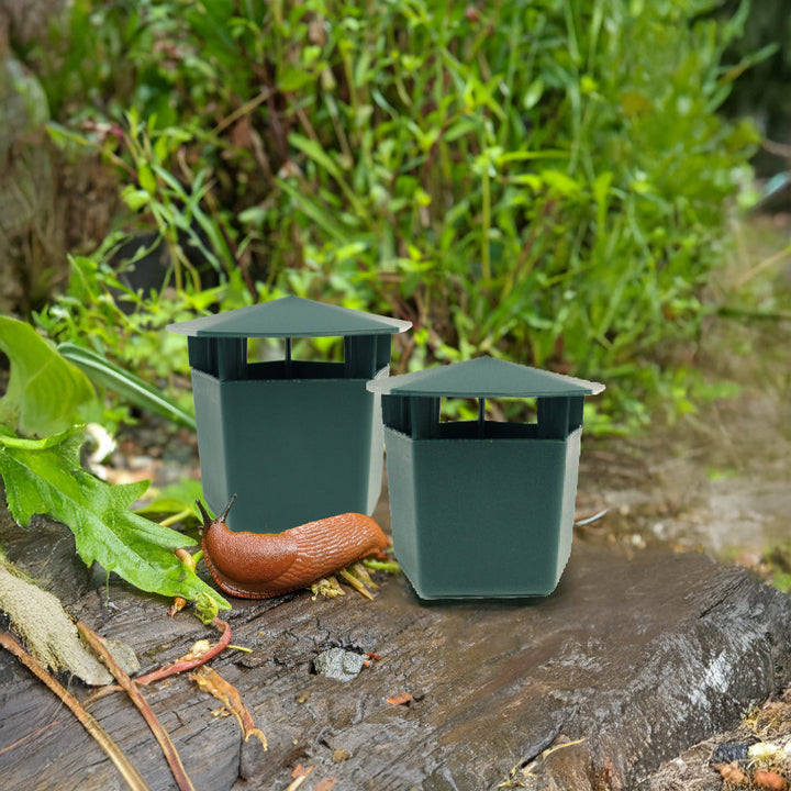 Two green plastic slug traps on a garden log with a slug nearby, surrounded by greenery.