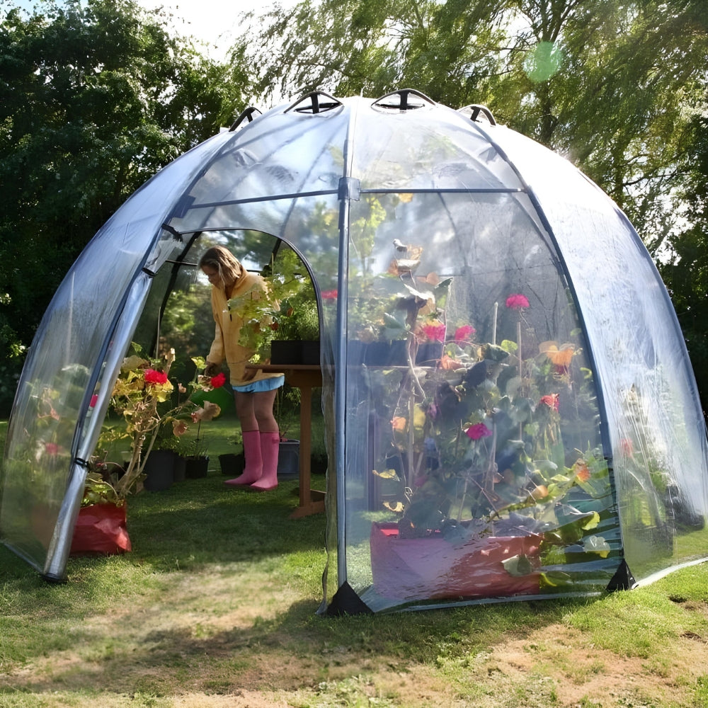 A transparent greenhouse dome with a family inside sitting around a table, with plants and a dog in the foreground.