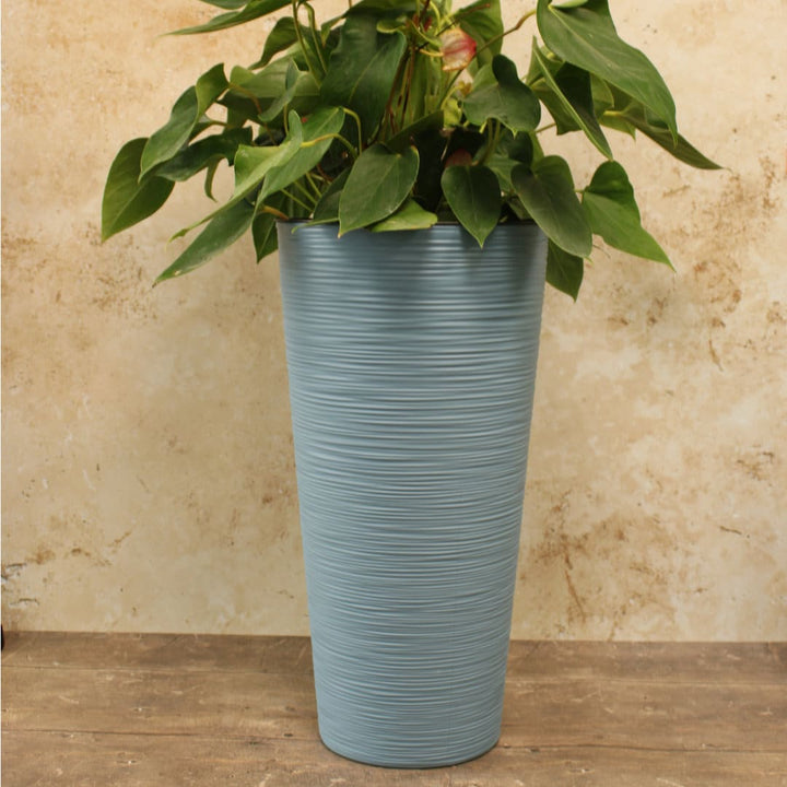 Tall blue plant pot with a plant on a wooden floor