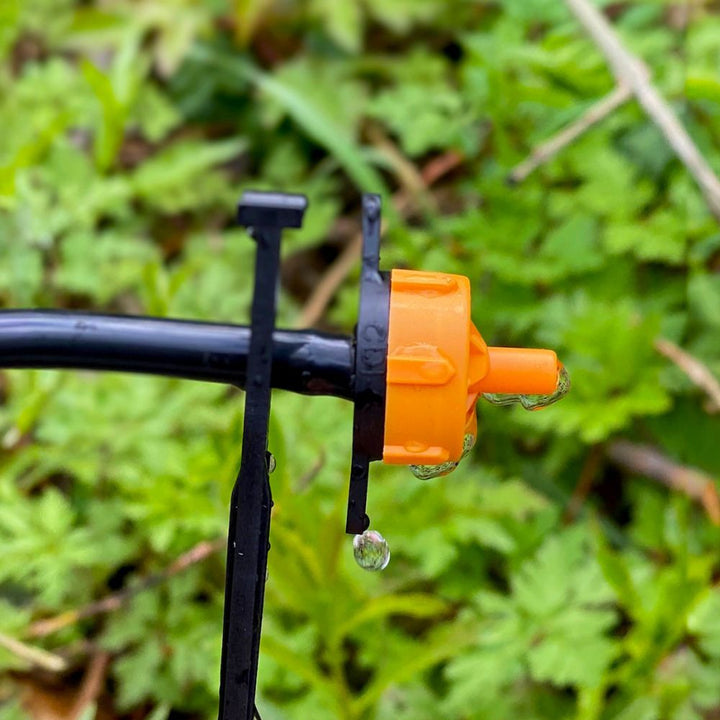 Close-up of an orange garden sprinkler head with water droplets on a green leafy background