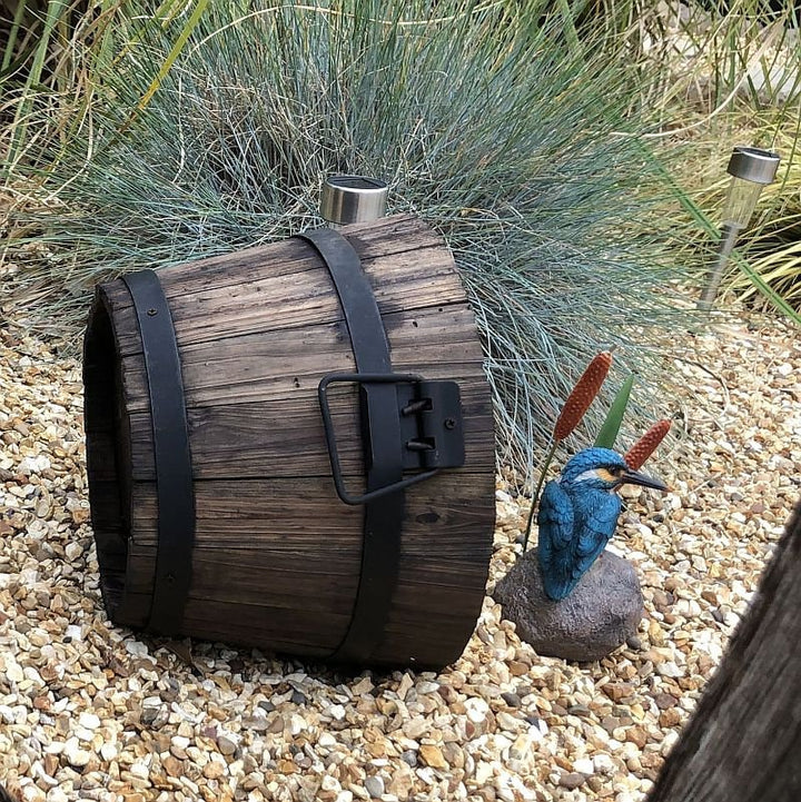 A rustic burnt wooden barrel garden planter with black barrel rings, placed on a gravel surface 